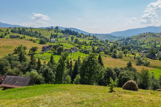 a Ukrainian Carpathian village in a valley with single houses and a green carpet of herbs