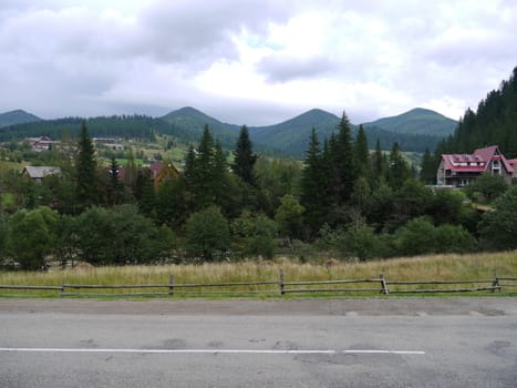 village by the road among the mountains surrounded by green trees under the cloudy sky. place of rest, tourism, picnic