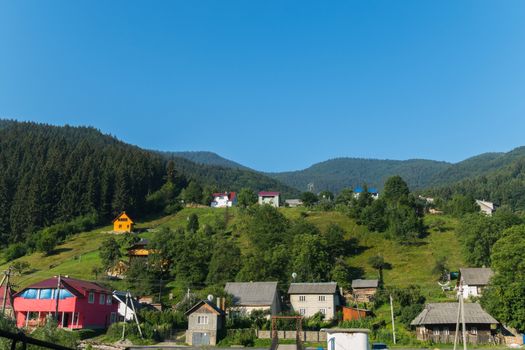 Carpathian village with large houses on hills in the background of spruce forests on the mountains