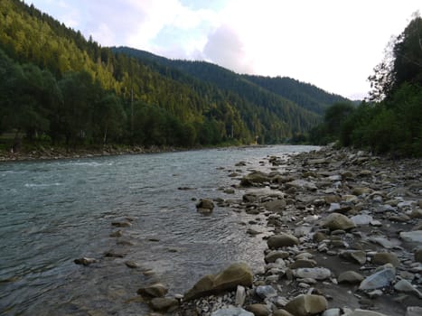 a shallow mountain river with clear water strewn with stones running between picturesque green slopes