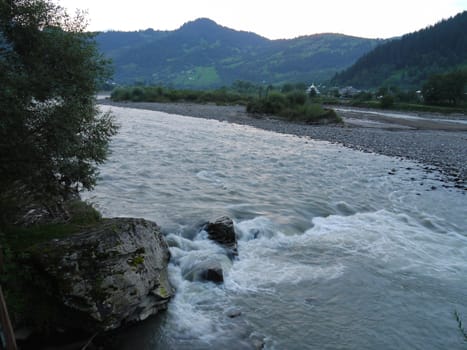 Fast, swift river flow against the backdrop of village houses at the foot of a large mountain