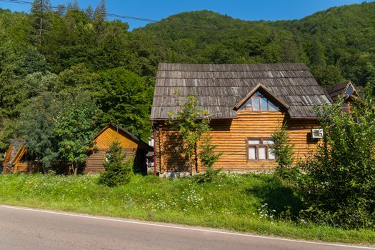 Authentic house of a wooden log house located right next to the road against the backdrop of a green mountain and blue sky