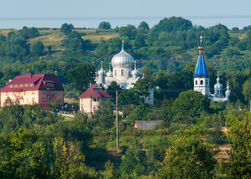 The tops of church temples with colorful roofs and domes against the background of green mountain slopes