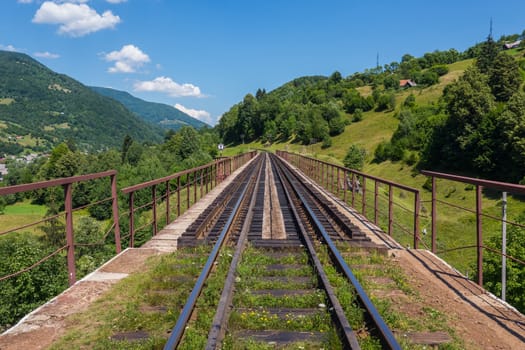 Old iron bridge with rails against the background of green trees and huge mountains