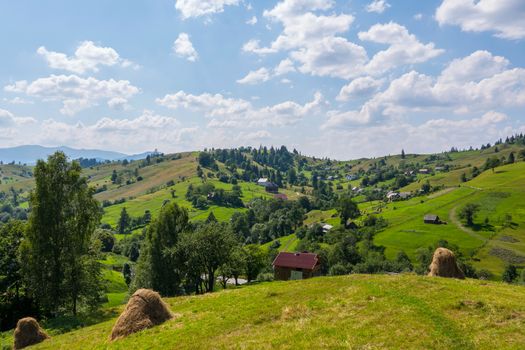 Green mountain plain with small rural houses and benches against the blue sky with white clouds