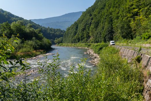 A winding road along the fast river against the backdrop of the orgomous green mountain ranges