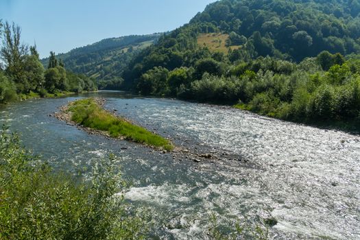 a refreshing river running at the foot of a mountain between low green beaches