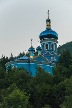 blue orthodox church among green tall trees under a blue cloudless sky