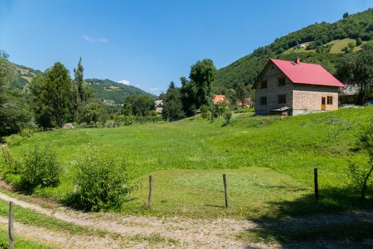 A rural road running next to the yard with a green lawn and a house standing in the depths on the hill.