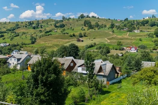 a village on a valley with scattered colored houses on green grass and trees near them