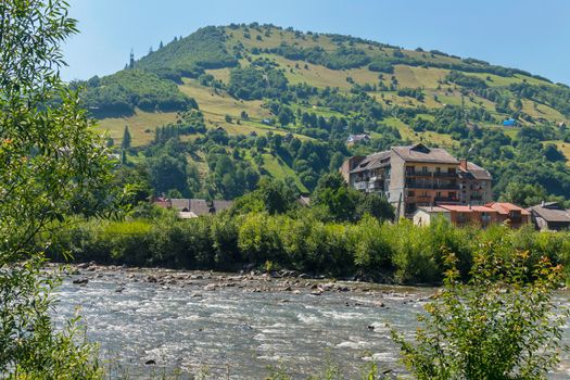 High houses with balconies and small traditional huts on the shore of a swift river at the foot of a big mountain