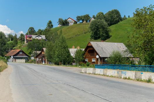 A wide asphalt road with large beautiful cottages and small rural houses on each side