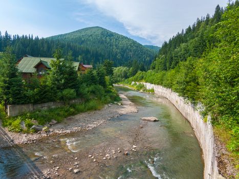 A stream with clear water enveloping the house and carrying its waters towards the mountain in the distance