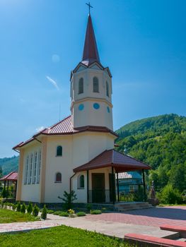 Beautiful modern church with a red roof and a big tower on a background of a green mountain