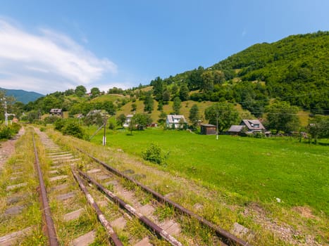 Old railway near small rural houses against the background of high green mountains