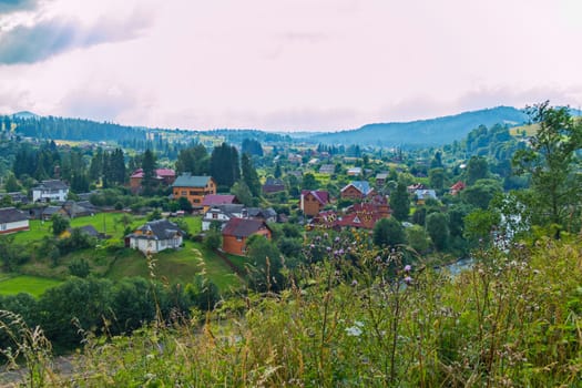 Top view of a small village with wooden houses near the river and the green mountain