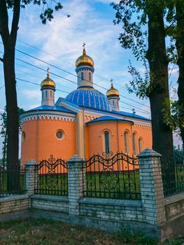Church with a blue roof and golden domes on a background of tall trees and a blue sky