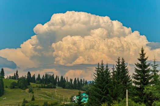 a huge white cloud on a blue sky hangs over a mountain village