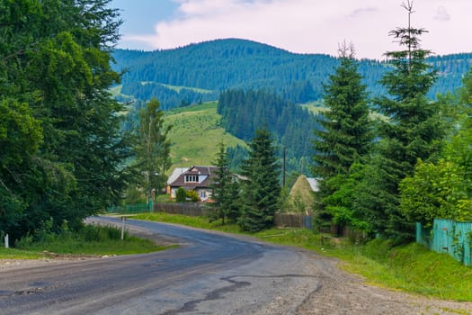 A steep winding road against the background of rural houses and huge green mountains