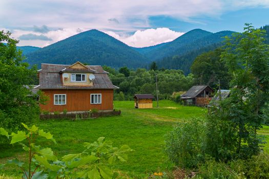 A small rural house with a courtyard and an old well against the background of green mountains and white clouds