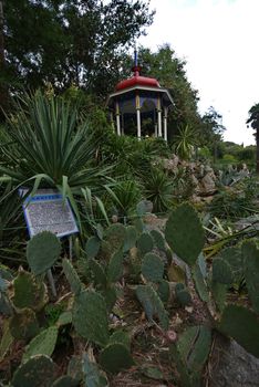 A flower bed with a lot of cacti and an oriental style gazebo with a red roof