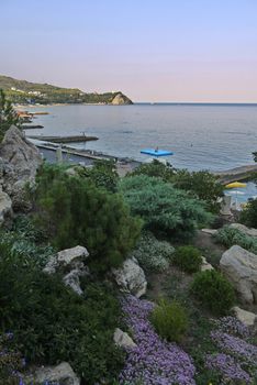 A beautiful view of the sea coast with large stones of small flowers piers coming out into the sea and seen in the distance a small rock.