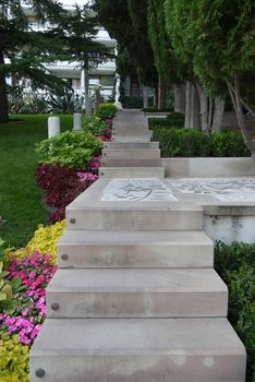 A staircase made of large concrete slabs leading to the house through a flower bed and a lawn with a garden