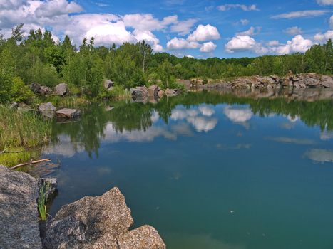 The banks of the lake are lined with large stone blocks in which the white clouds are reflected on the blue sky