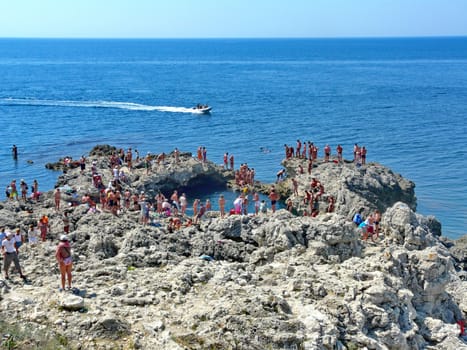 rocky people filled with a sea shore and a motor boat sailing to the shore along the blue calm sea under a cloudless sky. resting-place