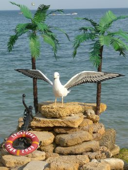 a statue of a white gull with palm trees on the background of a blue sea in Evpatoria