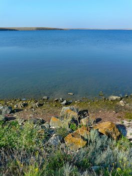The sharp stones are covered with green moss on the shore of a transparent blue lake