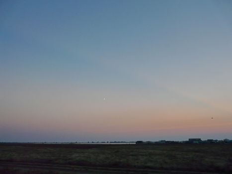 a small thin haze of the moon in a clean purple sky above the deserted spaces