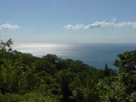 A magnificent landscape stretching away to the horizon line of the sea with a blue sky on it and rare clouds and an iodine boat sailing along the shore.