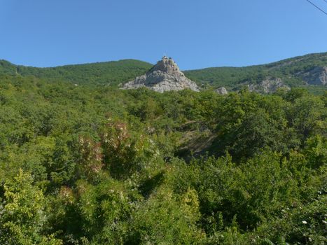 a rocky summit with a monument in the middle of the overgrown trees of the hills