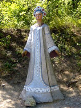 Sculpture of the fairy-tale character Vasilisa the Beautiful against the background of green deciduous trees