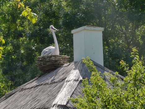 Decorative stork in a wicker nest near the smoke on the roof of the old Ukrainian house