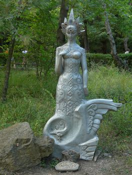 Stone sculpture of the heroine of the fairy tales of the Swan Princess against the background of the green park zone