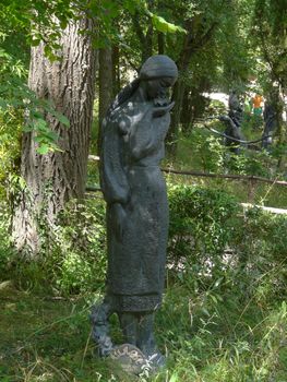 A statue of a fragile woman with a lily in her arms in a park under a tree. Exhibition for tourists