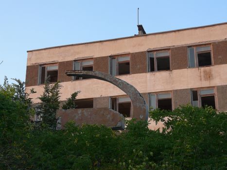 Sickle and hammer standing in green bushes against the ruined building