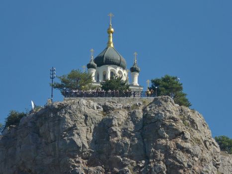 A small church with an observation deck on the top of a rocky rock on the background of a clear sky