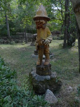 A wooden statue of a gnome with an umbrella in his hands stands on a rock in the park