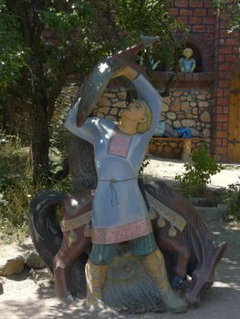 Multicolored sculpture of a fairy-tale character with a horse against the background of a green tree