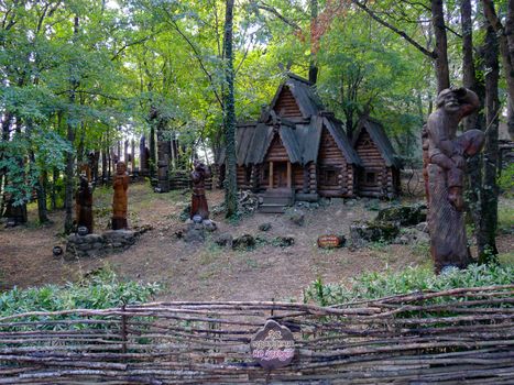 An old wooden log hut with carved statues and a fence-wattle fence among a thick deciduous forest. a fabulous resting place for the whole family