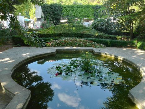 An artificial pond with lilies surrounded by a granite stone, and around a green flowerbed