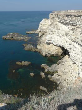 Sea coast with steep rocky slopes and canyons against the backdrop of the endless blue sky