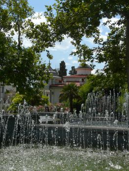 Transparent refreshing fountains with transparent water in the park with people on the benches resting.