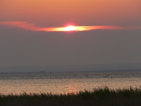 sunset sitting between clouds on a water surface with a small ripple
