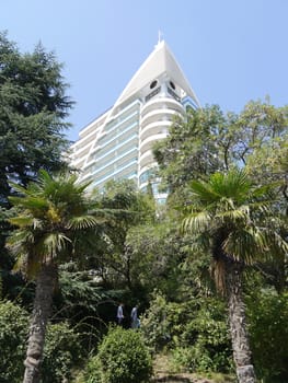 A high facade of a modern house with a chic architecture towering on green trees rising below.