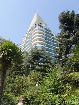 A modern white hotel with transparent blue balconies against the background of green exotic trees and palms