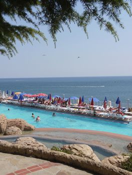 Swimming pool with tourists near the beach in the background of the endless blue sky